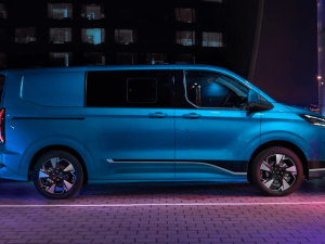 A side view of the All-New Ford Transit Custom DCIV in blue, parked in a car park at night, with electric style lights around the van.